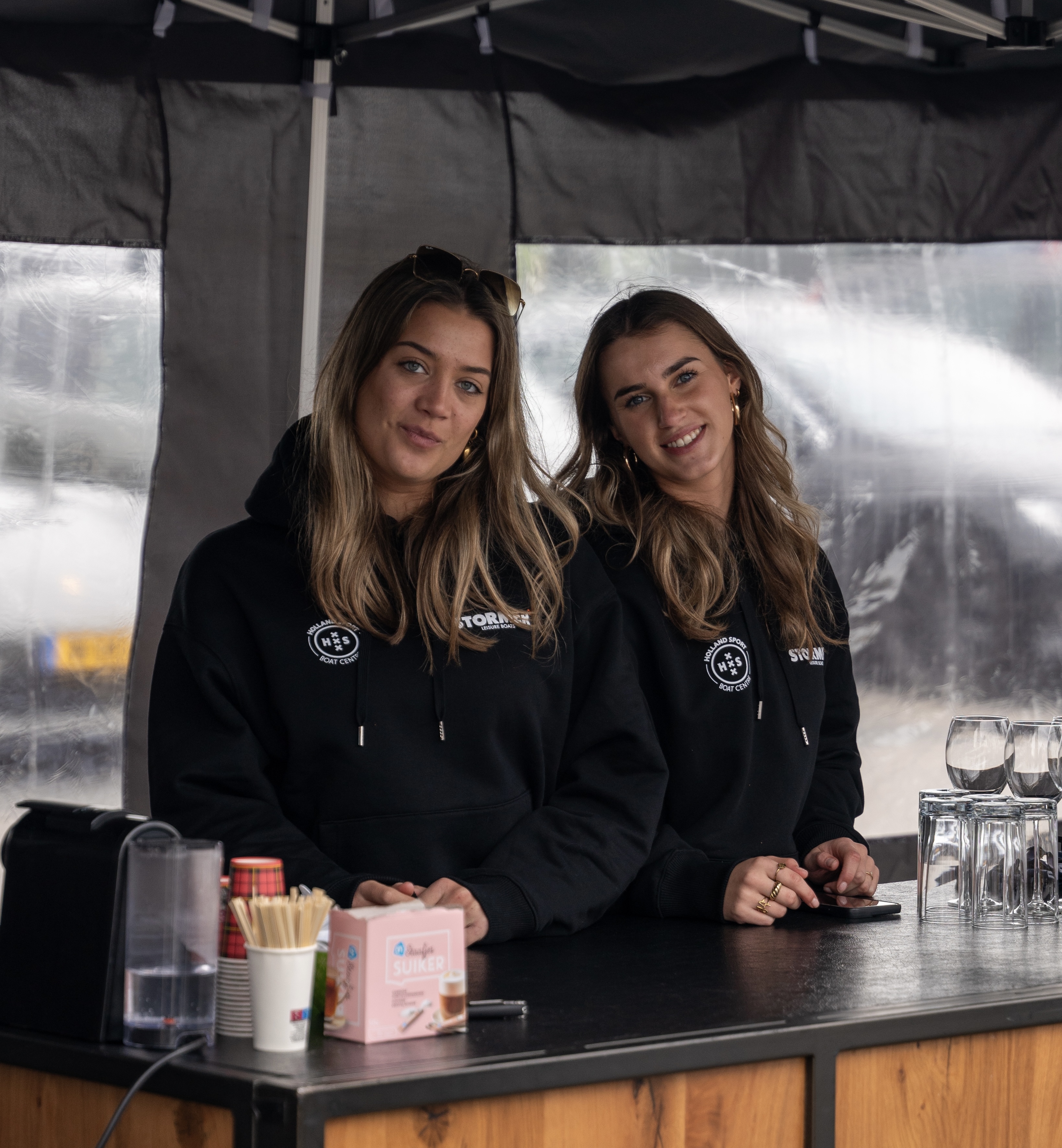 Twee vrolijke Crewmates in zwarte hoodies achter een professionele bar setup tijdens een event